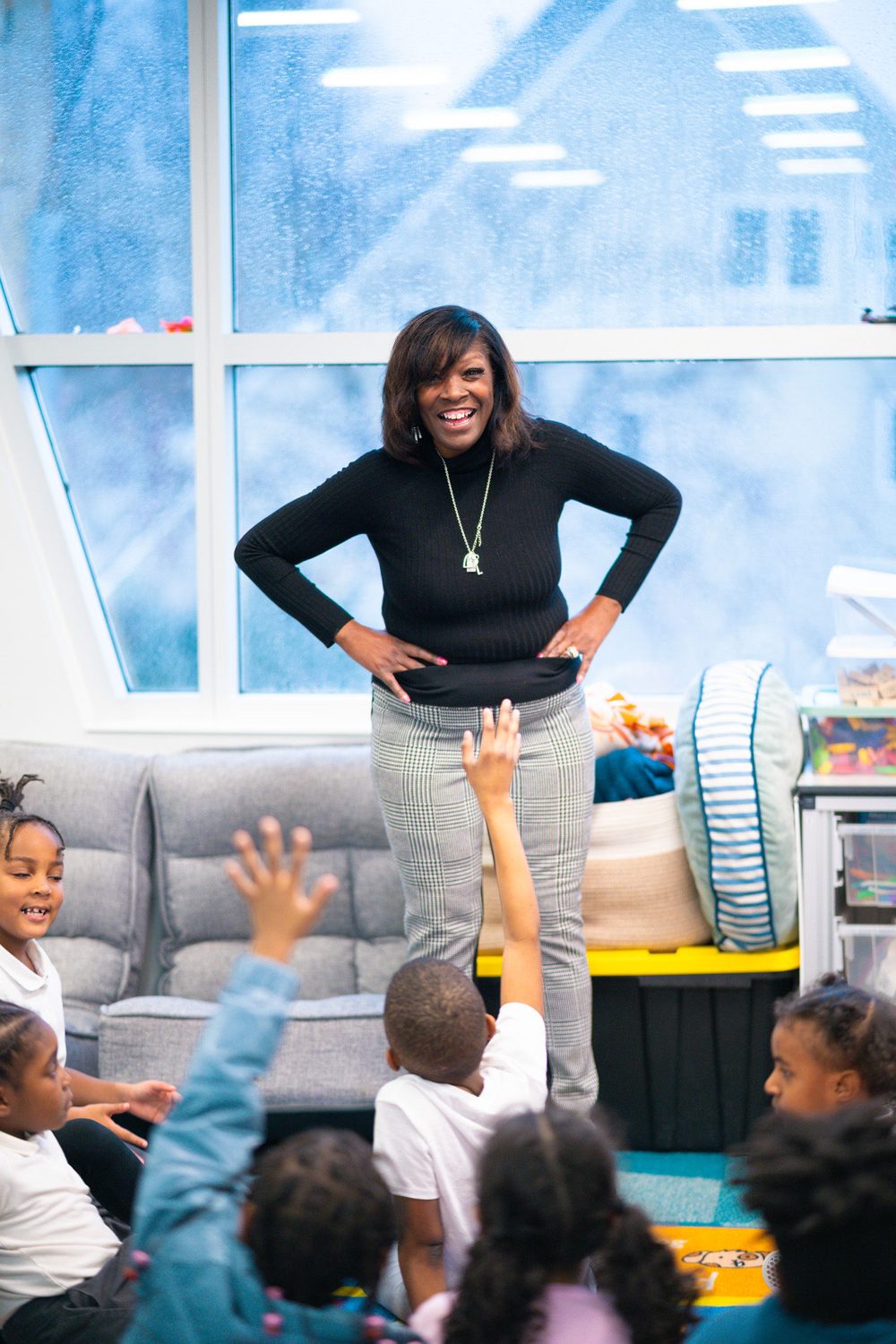 A teacher laughing with a room of students with raised hands